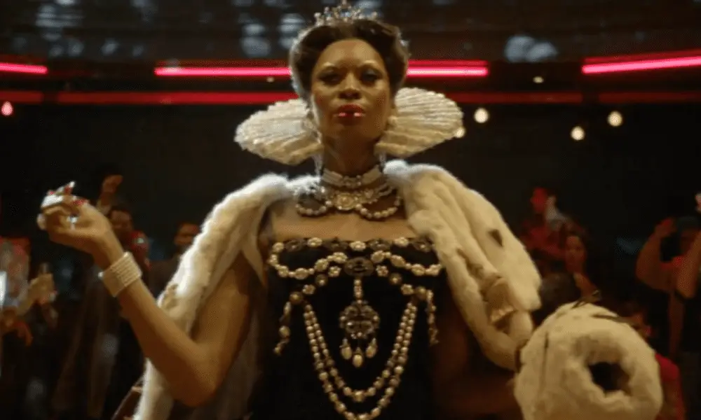 Elektra walks in the ball wearing a crown, white ruffled collar, bejeweled gown, and fur cape, that look like they are from 1600s European royalty.