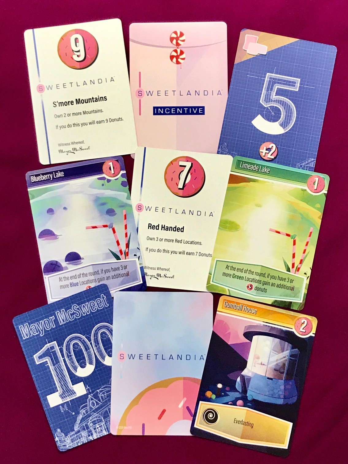 random assortment of cards from sweetlandia showing different locations, incentives, and bidding cards