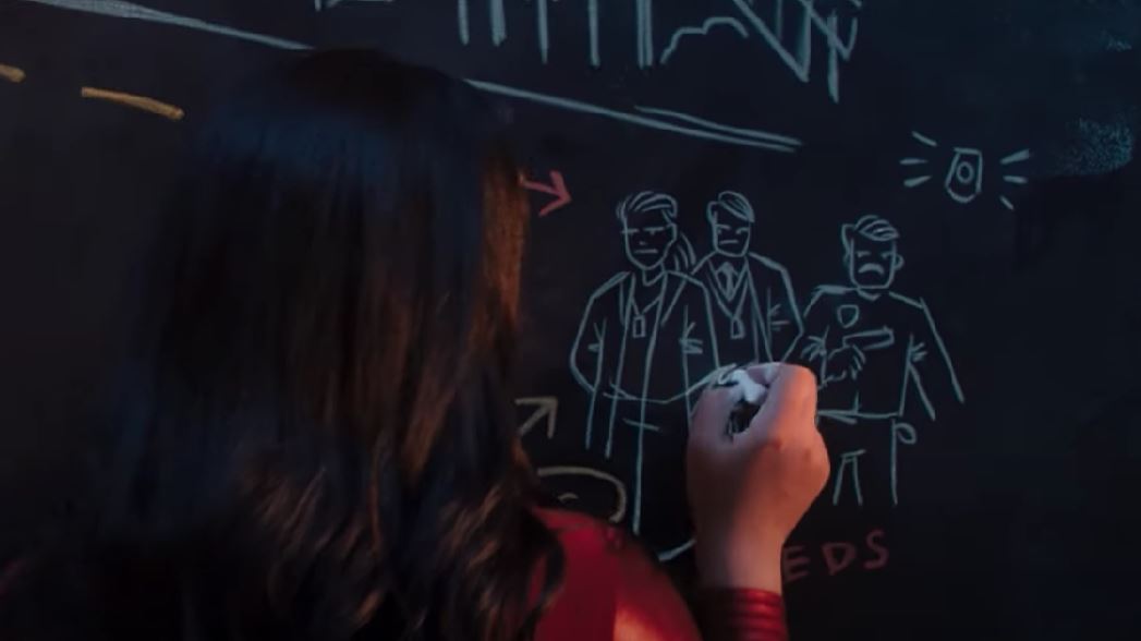 Ms. Marvel plotting on a chalkboard