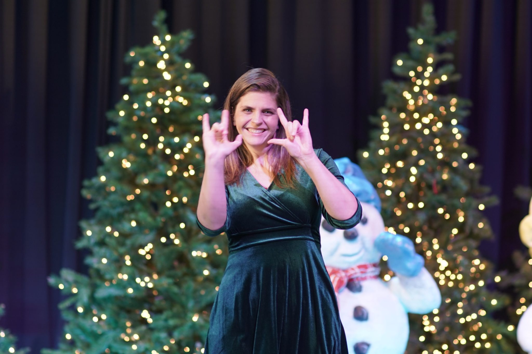 A white woman signing in front of Christmas trees in Merry & Gay