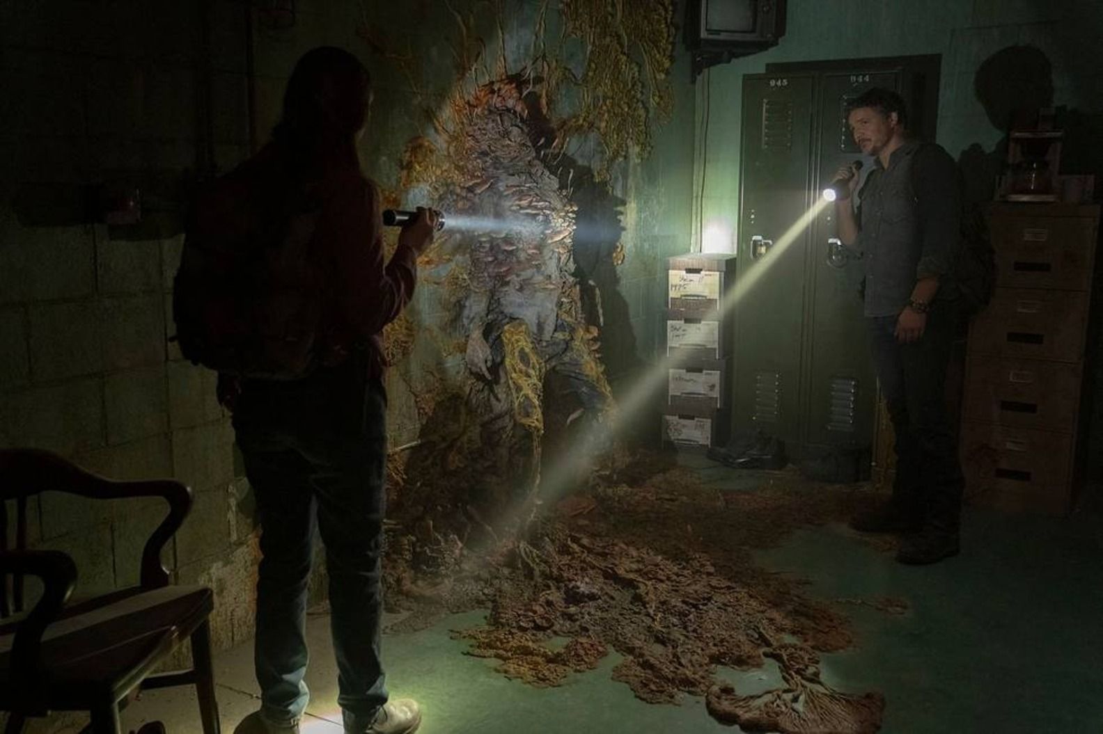 Joel and Tess stand in a room with a dead zombie. 