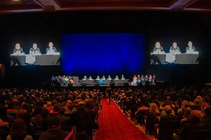 A packed auditorium where WGA and other union representatives are on stage.