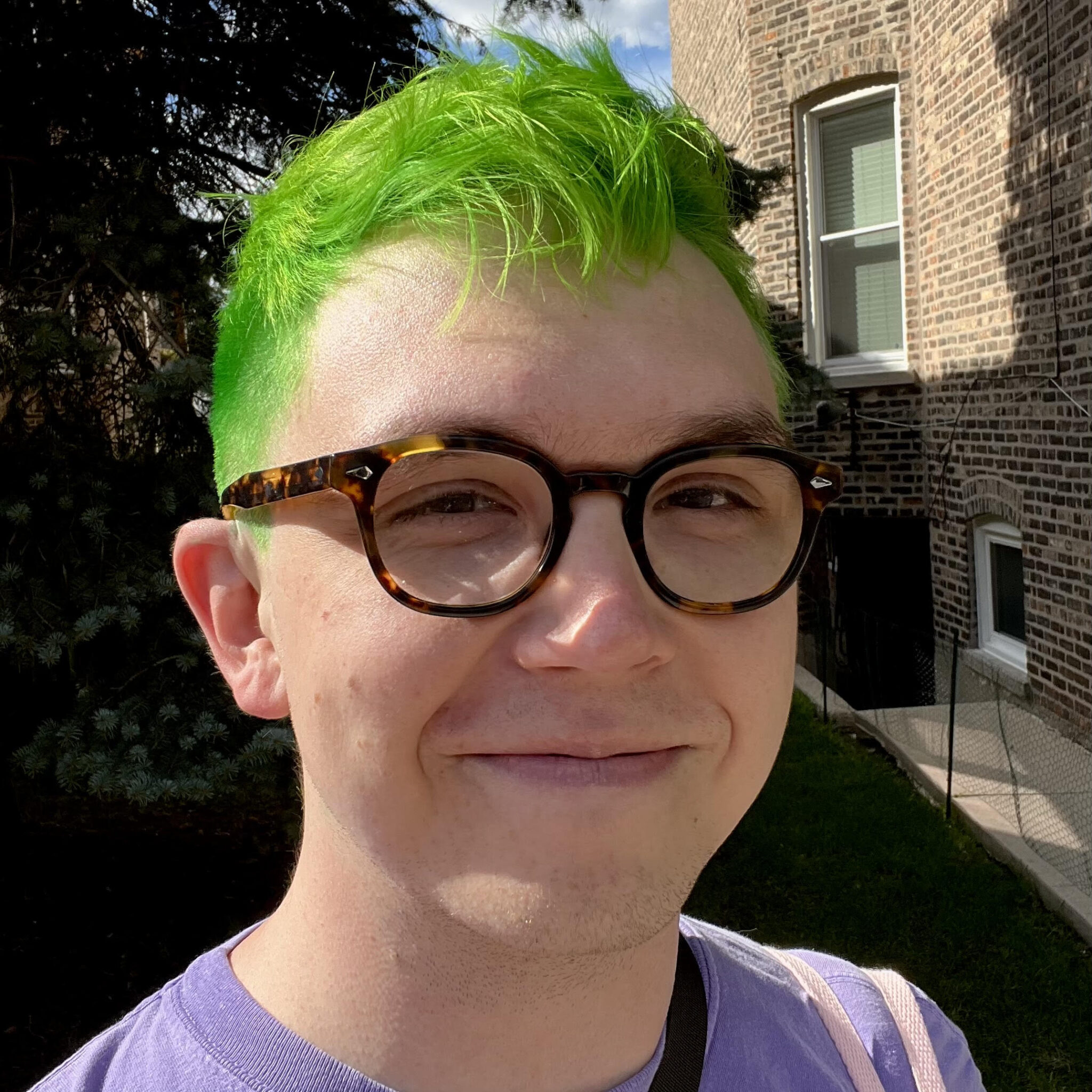A headshot of erik morrison, a white masc nonbinary person with tortoiseshell glasses and green hair