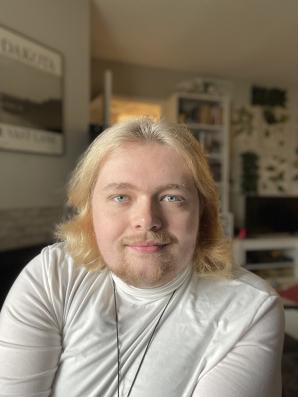'Off Screen' Episode One: Tony Kiger 1 An image of Tony. They have blonde mid length hair, and are wearing a white shirt