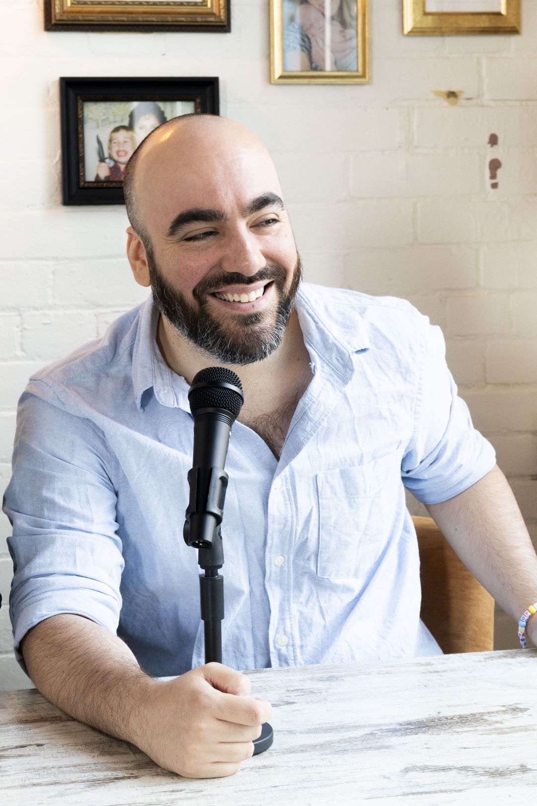 A man in a button down blue shirt, smiling, in front of a microphone.