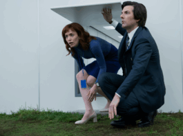 Helena and Mark crouched together as they enter a white room with grass. Apple+ Severance